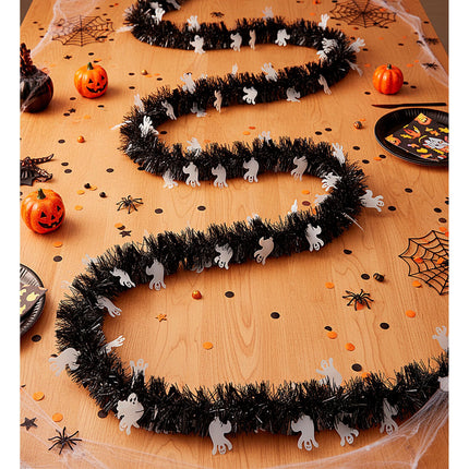 Geestjesslinger in S-vorm over een houten Halloweentafel met pompoenen en confetti