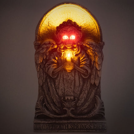 Grafsteen engel in het donker met rood oplichtende ogen en gloeiend kaarslicht voor Halloween