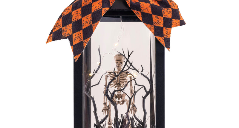 Halloween lantaarn zwart met skelet tussen kale takken, lichtjes en oranje-zwarte strik met schedeltje