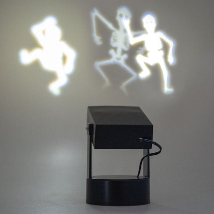 Halloween projector met dansende skeletten in werking, drie witte skeletsilhouetten op de wand tijdens Halloween