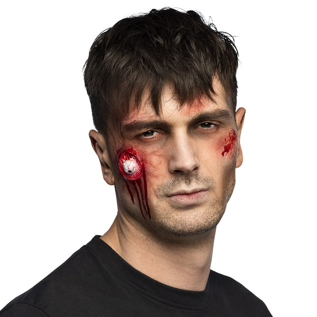 Latex wond met oogbalmotief op de wang met rode bloeddruppels, zombielook voor Halloween