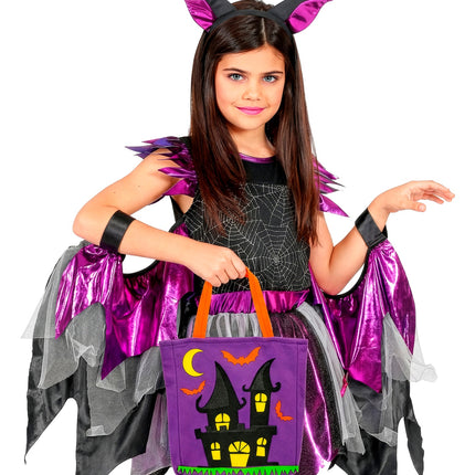 Meisje in vleermuiskostuum met paarse trick-or-treat tas met spookhuisopdruk