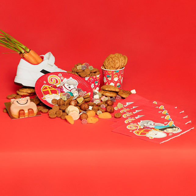 Papieren bordjes Sinterklaas tussen speculaas en snoepgoed op een rode feesttafel