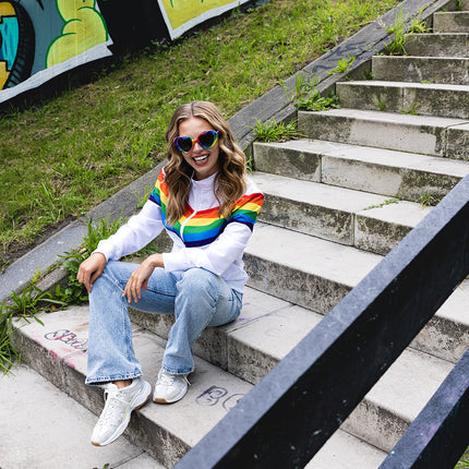 Regenboog trainingsjasje dames op een pridefeest, gecombineerd met jeans en witte sneakers