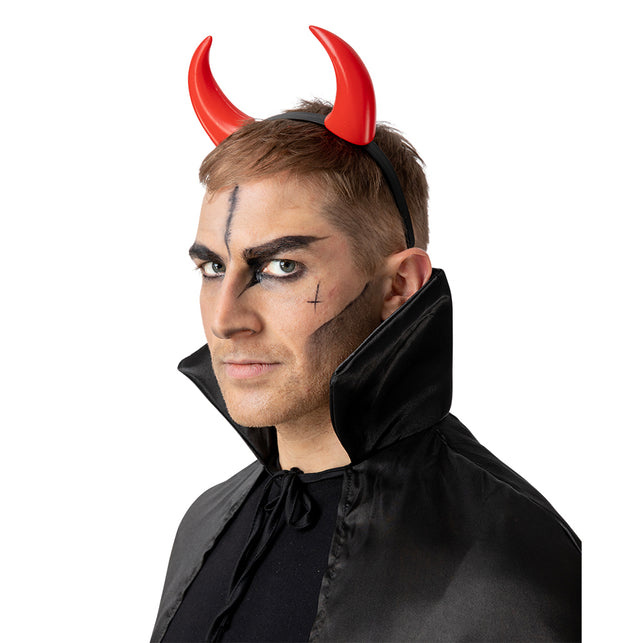 Rode duivelhoorntjes op haarband gedragen door een man met donkere duivelsschmink op Halloween