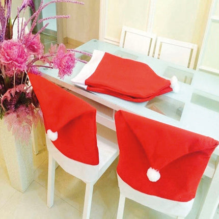 Rode kerstmuts stoelhoezen op witte stoelen, met opgevouwen exemplaren op de eettafel