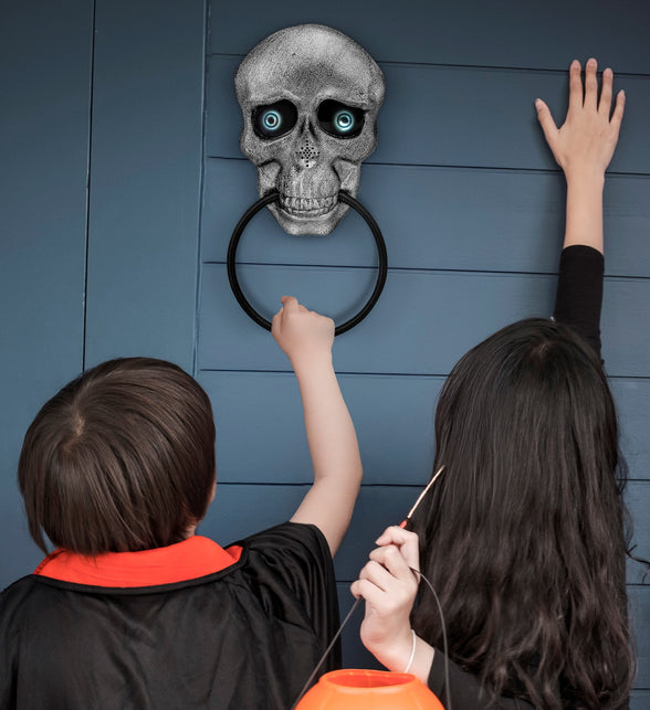 Schedel deurklopper aan blauwe voordeur terwijl kinderen op halloweenavond aan de ring trekken