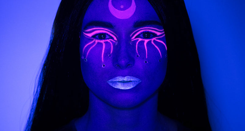UV schminkset heks onder blacklight: paars gezicht, roze maansikkel, oogpatroon en blauwe lippen voor Halloween